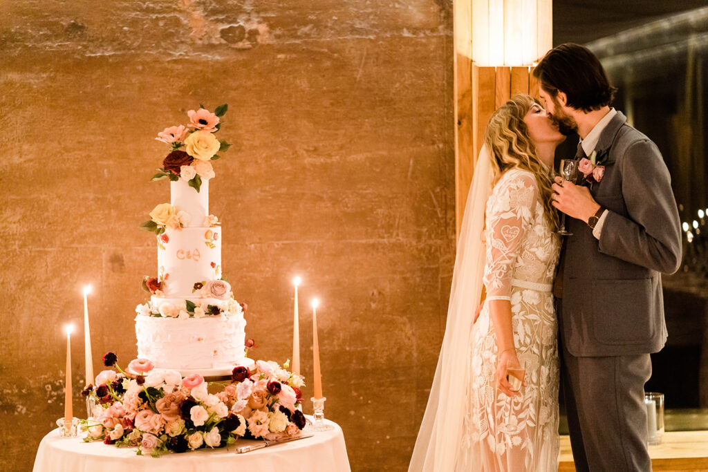 a pale pink floral wedding cake with lit candles either side and bride and groom
