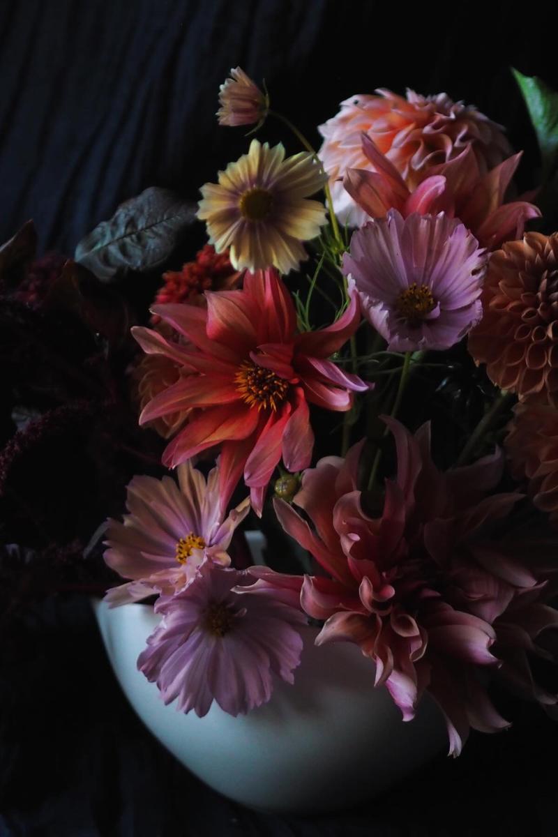 A dark and moody flower arrangement with dahlias, amaranthus and cosmos in peach, pink and orange