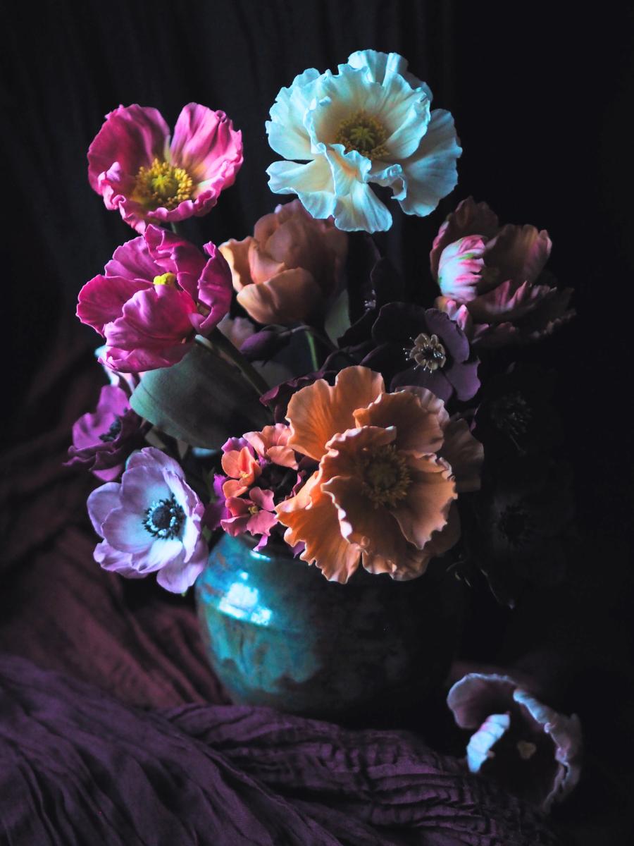 Moody Spring sugar flower arrangement in jewel colours including orange, pink and cream Iceland poppies, purple anemones, pink and peach wallflowers, pink and peach tulips and deep red hellebores against a dark background